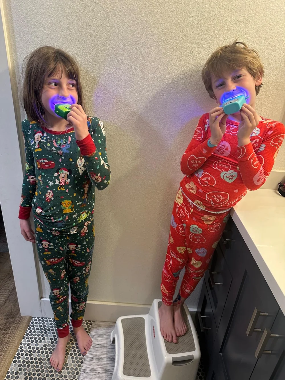 Two siblings brushing at the bathroom sink with their light-up U-shaped brushes